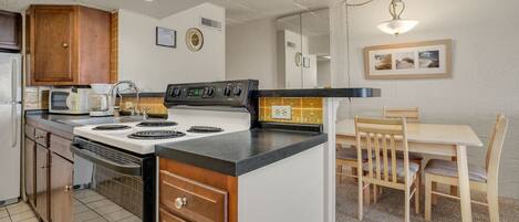 A kitchen with a stove, microwave, and cabinets. There is a dining table with chairs and a chandelier.