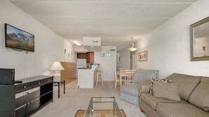 Una sala de estar con un sofá, una mesa de centro, un televisor y una cocina al fondo.