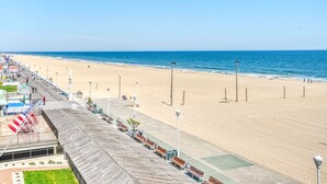 Un paseo marítimo con bancos e faroles que conduce a una playa arenosa con el océano al fondo.