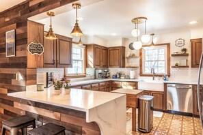 Une cuisine moderne avec des éléments en bois, des plans de travail en marbre blanc, des appareils électroménagers en acier inoxydable et des luminaires suspendus.
