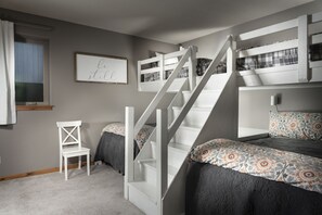 A bedroom with bunk beds, a staircase, a small white chair, and a framed inspirational quote on the wall.