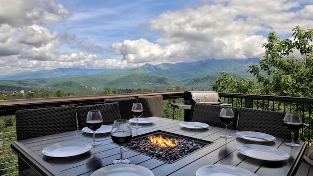 An outdoor dining area with a fire feature, surrounded by wicker furniture and overlooking a mountainous landscape.