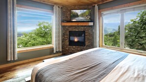 A bedroom with a stone fireplace, large windows, and a bed.