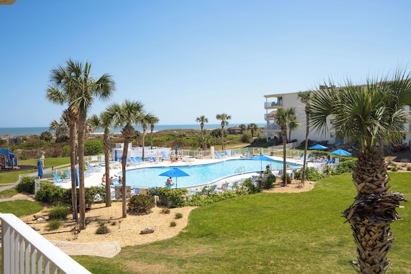 Zona de piscina con palmeras, cielo despejado y vista al océano.