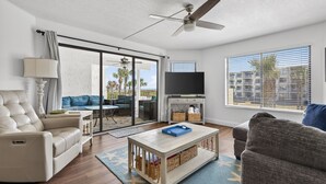 A living room with a sofa, a coffee table, a TV, and a balcony with a view. - CRC 2208 - Oceanview Condo (St Augustine)
