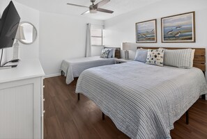 Ein Schlafzimmer mit zwei Betten, einem Deckenventilator, einem Fernseher und Bildern an der Wand.