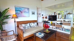 Un salon chaleureux avec un canapé, une table basse, un téléviseur et une bibliothèque remplie de livres et d’objets décoratifs.