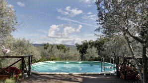 A wooden deck leading to a rectangular swimming pool with a view of mountains and trees. - Ricavo lodge with heated pool and outdoor jacuzzi (Lecchi in Chianti)