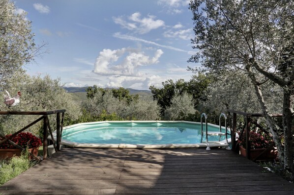 A wooden deck leading to a rectangular swimming pool with a view of mountains and trees. - Ricavo lodge with heated pool and outdoor jacuzzi (Lecchi in Chianti)