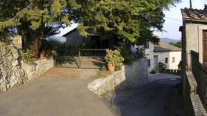A stone wall with a sign, a paved path, and a gate leading to a building with a tiled roof. - Ricavo lodge with heated pool and outdoor jacuzzi (Lecchi in Chianti)