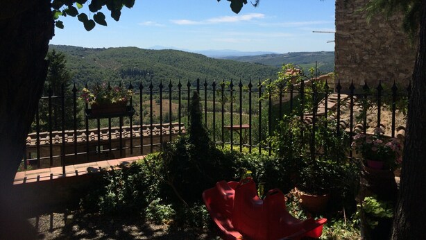 A view through a stone wall with a metal fence, overlooking a valley with greenery and distant hills. - Ricavo lodge with heated pool and outdoor jacuzzi (Lecchi in Chianti)