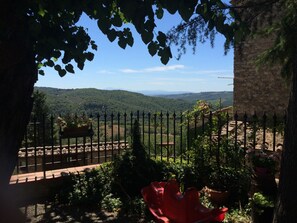 A view through a stone wall with a metal fence, overlooking a valley with greenery and distant hills. - Ricavo lodge with heated pool and outdoor jacuzzi (Lecchi in Chianti)