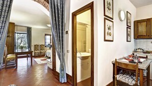 A spacious room with a wooden floor, a dining table, a kitchen area with cabinets, and a bathroom visible through an archway. - Ricavo lodge with heated pool and outdoor jacuzzi (Lecchi in Chianti)