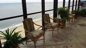 Ein Balkon mit Korbstühlen und Topfpflanzen mit Blick auf einen Strand.