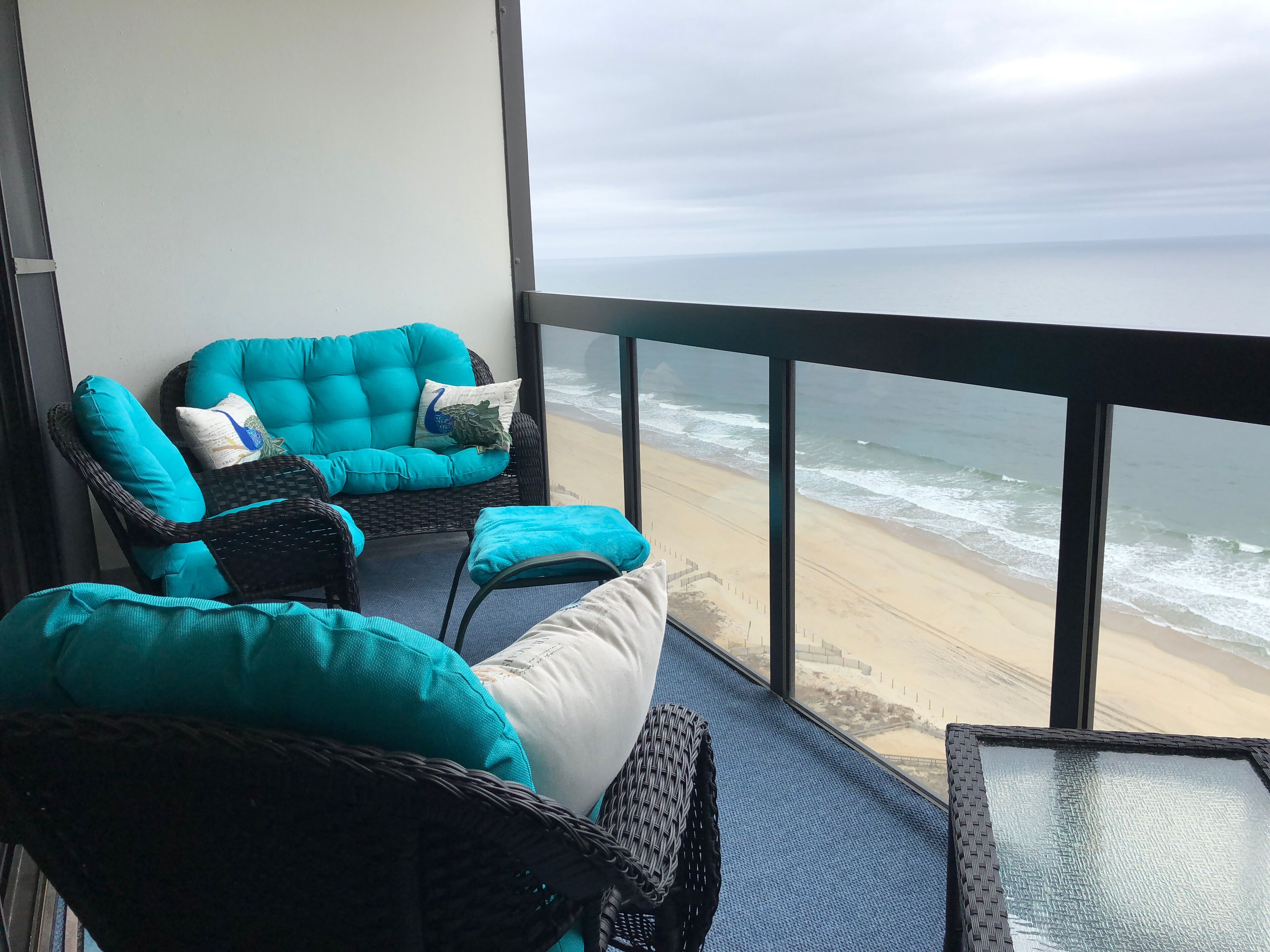 Een balkon met rieten meubilair en uitzicht op het strand.