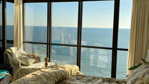 Ein Zimmer mit einem großen Bett, einem Sessel und Meerblick durch große Fenster.