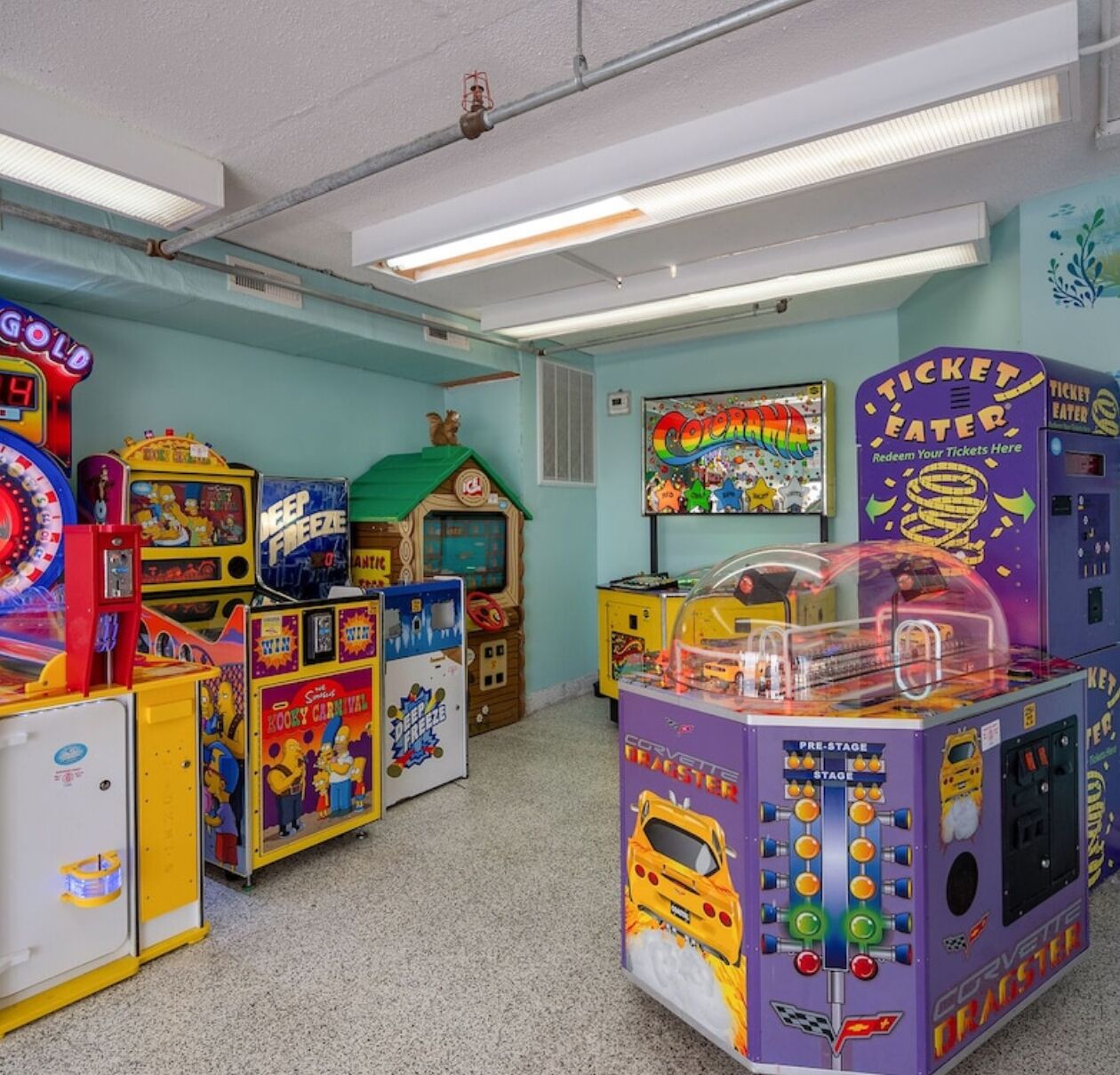On y trouve une variété de jeux d’arcade, dont un jeu de course de type « dragster » avec une Corvette, dans une pièce aux couleurs vives, avec des murs de couleur turquoise et un toit vert.