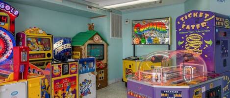 On y trouve une variété de jeux d’arcade, dont un jeu de course de type « dragster » avec une Corvette, dans une pièce aux couleurs vives, avec des murs de couleur turquoise et un toit vert.