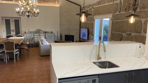 A modern kitchen with a built-in dishwasher, a stone wall, a chandelier, and a dining area with antique furniture. - Villa 15 minutes from Porto  (Paredes, Carvalhal)
