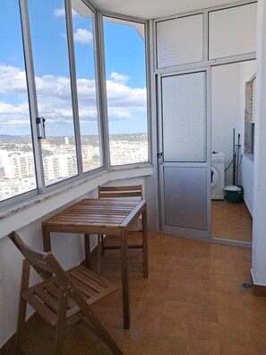 A balcony with a view of a cityscape, a wooden table, and a door leading to a laundry area. - TORRE 17- City View, Wifi, Cozy and Refurbished (Quarteira)
