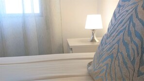 A bed with a white headboard, a bedside table with a lamp, and a window with curtains. - TORRE 17- City View, Wifi, Cozy and Refurbished (Quarteira)