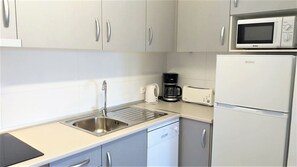 Cozinha compacta com armários brancos, pia de aço inoxidável, cafeteira, torradeira e geladeira.
