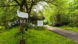 A signpost with 'Portneullan' written on it, a path leading through a wooded area, and a signboard with text.
