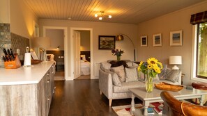 A well-lit living area with a sofa, coffee table, and a dining table. There is a kitchen area with a counter and a dining table. The room has a wooden floor and a ceiling with recessed lighting. - Beautiful 4 star, 2 bedroom chalet with stunning loch and mountain views (Crianlarich)