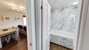 Una habitación con pared de mármol, suelo de madera, puerta blanca e iluminación empotrada en el techo.