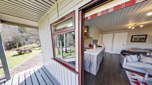 Un patio cubierto con piso de madera, una zona de comedor con mesa de picnic y una cocina con encimera blanca y sofá.