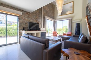 Ein modernes Wohnzimmer mit großem Flachbildfernseher, Ledersofas, einem Holztisch und einer Treppe.