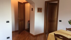 A room with wooden flooring, a dining table with a yellow tablecloth, and two wooden doors. - Panoramic apartment in Lake Como area (Asso)