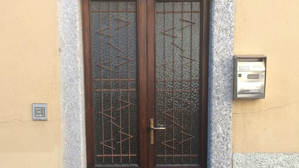 A double wooden door with a metal grid pattern, a mailbox, and a house number '20' on the wall. - Panoramic apartment in Lake Como area (Asso)