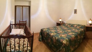 A bedroom with a wooden crib, a bed with floral bedding, two bedside tables with lamps, and a small framed picture on the wall. - Panoramic apartment in Lake Como area (Asso)