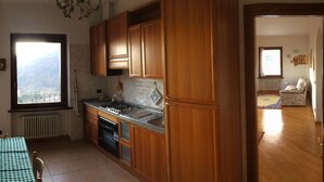 A compact kitchen with wooden cabinets, a gas stove, and a window with a view. - Panoramic apartment in Lake Como area (Asso)