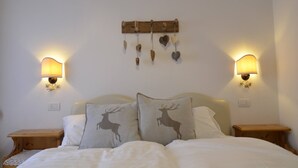 Un dormitorio con una cama, dos mesitas de noche, un perchero de madera en la pared con objetos colgando y lámparas de pared.