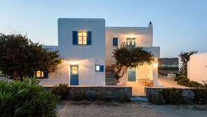 A two-story building with a stone staircase leading to the entrance, a small outdoor seating area, and a view of the landscape in the background. - Beachfront - Authentic- Idyllic- Relaxing -Homey - Sleeps 9 - Close to Naoussa  (Paros)