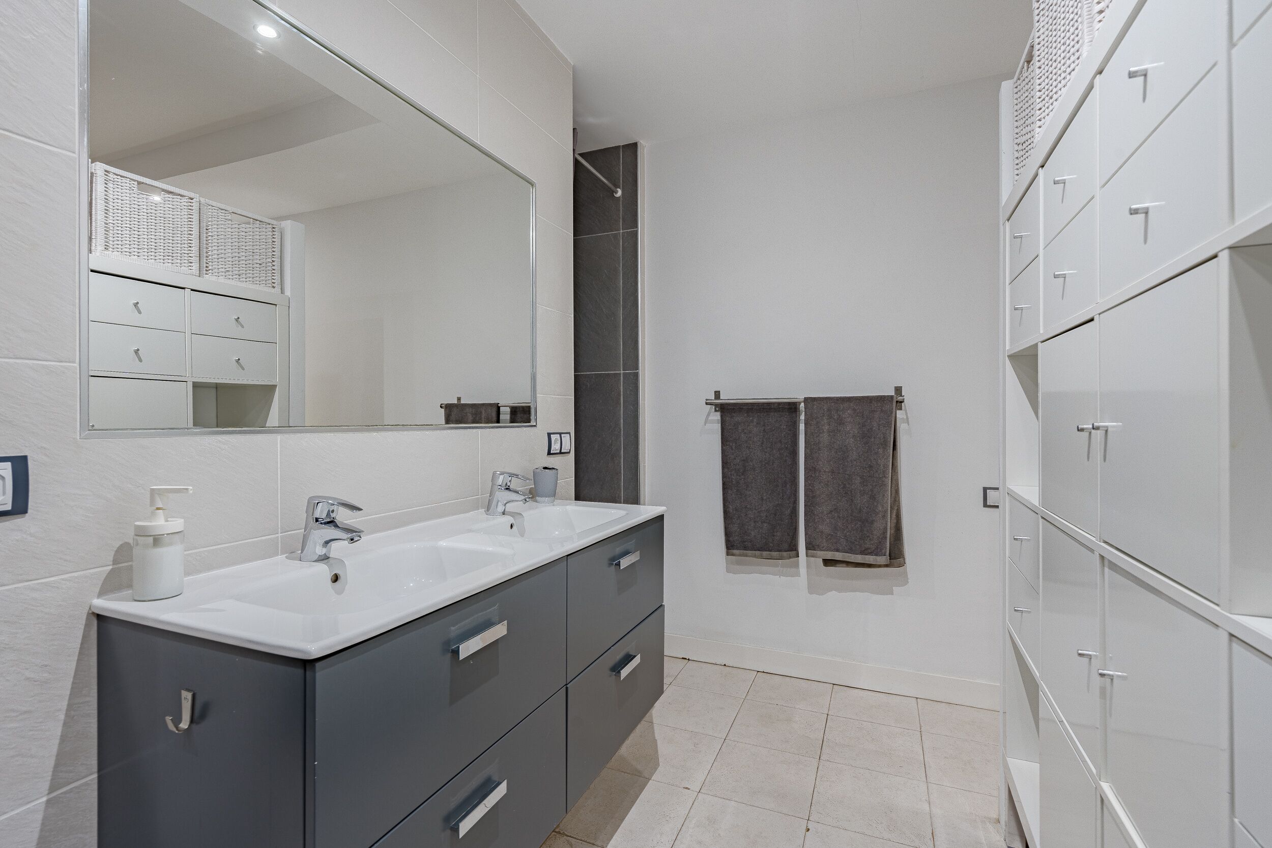 A modern bathroom with two sinks, a large mirror, and a walk-in shower.