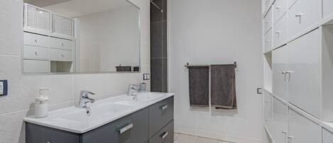 A modern bathroom with two sinks, a large mirror, and a walk-in shower.