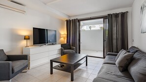Un saló modern amb un sofà, una taula de centre, una televisió i una porta corredissa de vidre que dona a un espai exterior.