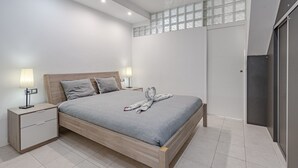 Un dormitori modern amb un llit de fusta, dues taules de nit amb làmpades, una finestra gran amb vistes i una porta corredissa.