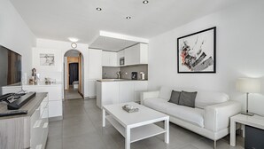 Un saló modern amb un sofà blanc, una taula de centre i una cuina al fons.