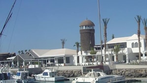 Un puerto deportivo con barcos amarrados, una torre de agua y una hilera de edificios blancos con un espacio cubierto.