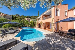 A swimming pool with lounge chairs and umbrellas, surrounded by a stone patio and a building with balconies. - House / Villa - LES ISSAMBRES (Roquebrune-Sur-Argens)
