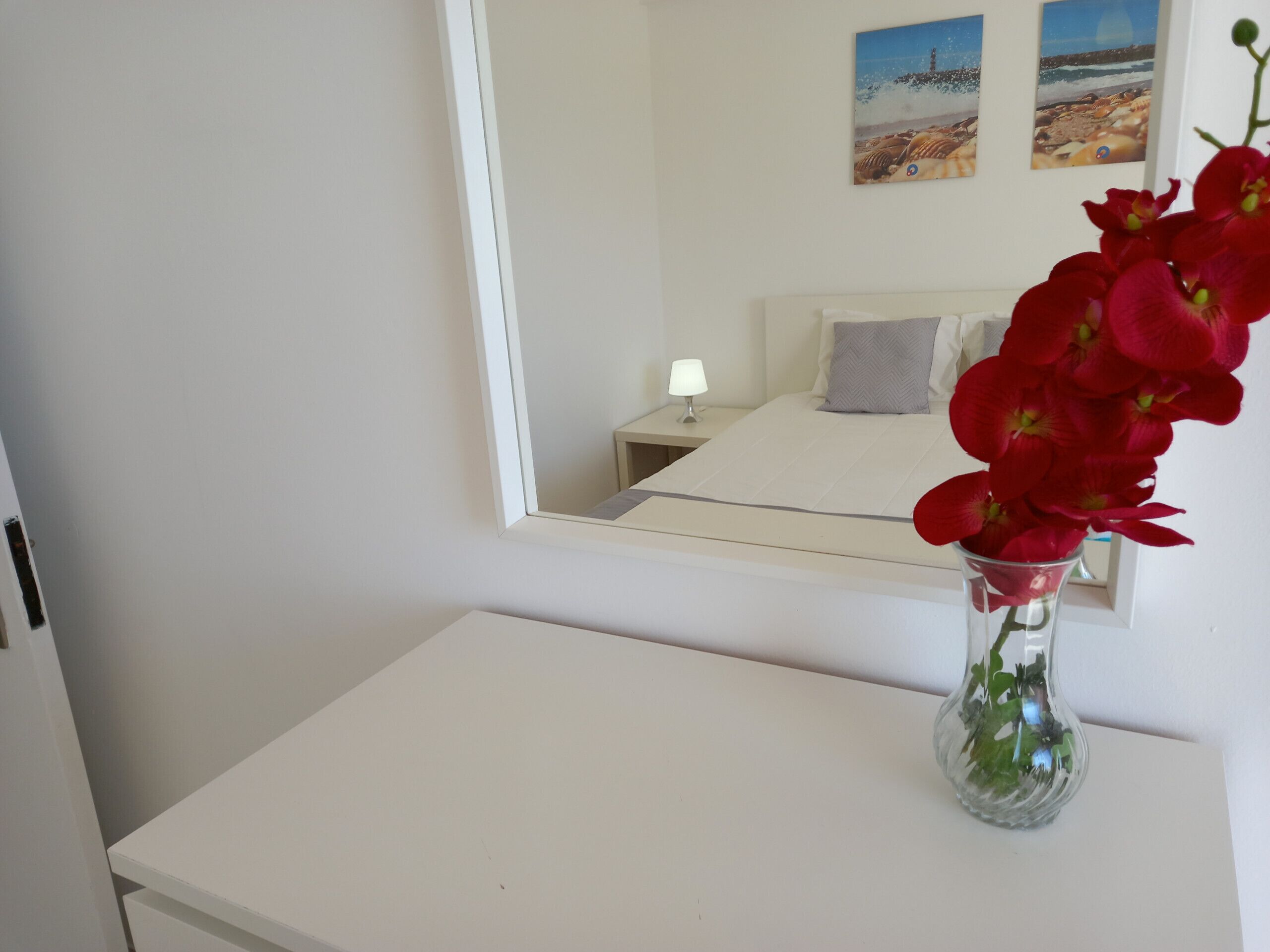 Une chambre d’hôtel avec un lit, une table de chevet avec une lampe et un vase rempli de fleurs rouges.