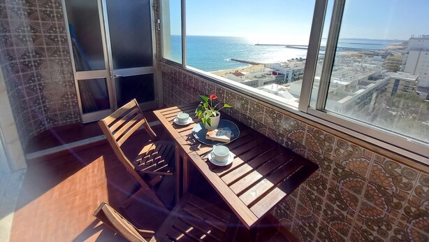 A balcony with a wooden table, chairs, and a potted plant. - TORRE AZUL- Magnificent Sunset, Wifi, 20 m from the Beach (Quarteira)