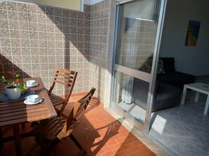 A sunlit patio with a wooden table, chairs, and a potted plant.