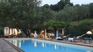 A swimming pool with lounge chairs and tables, surrounded by trees and a stone pathway.