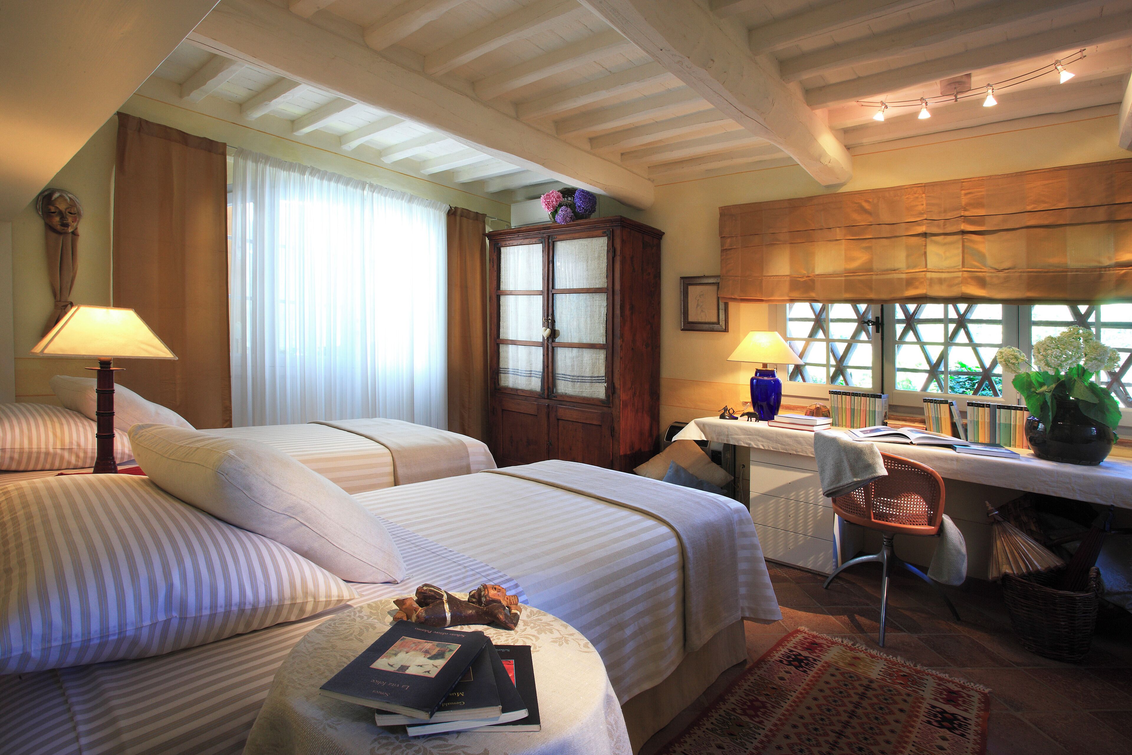 Habitación de hotel con dos camas, un escritorio, una silla, una ventana con cortinas y una estantería.