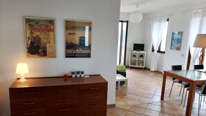 A modern living room with a wooden cabinet, a glass dining table, and a TV on a white stand.